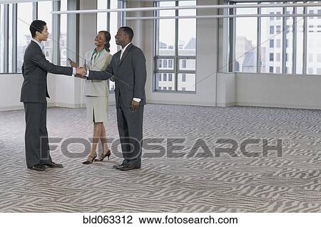 Stock Image - Multi-ethnic business people handshaking in empty building. Fotosearch