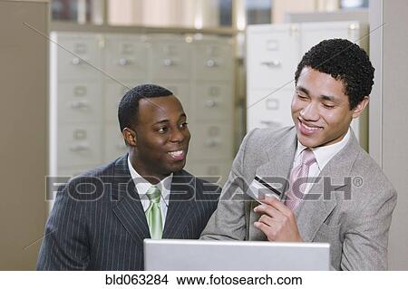Multi-ethnic businessmen with laptop holding credit card View Large Photo Image Picture - Multi-ethnic businessmen with laptop holding credit card. Fotosearch