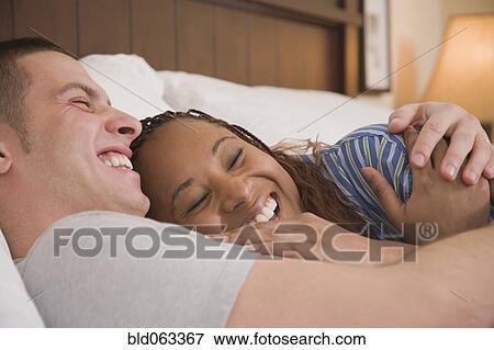 Stock Photo - Multi-ethnic couple laughing in bed. Fotosearch