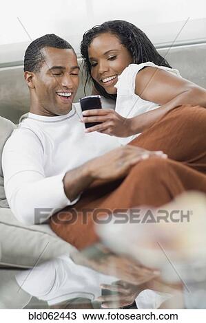 Multi-ethnic couple laying on sofa looking at cell phone View Large Photo Image Stock Image - Multi-ethnic couple laying on sofa looking at cell phone. Fotosearch