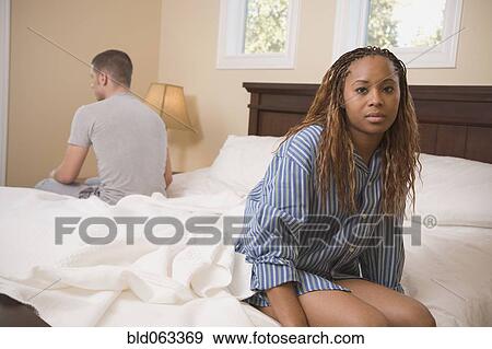 Stock Photo - Multi-ethnic couple sitting at opposite edges of bed. Fotosearch