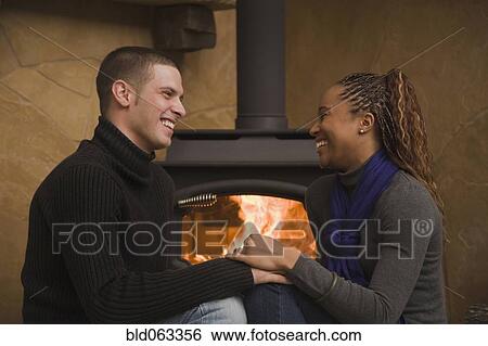Stock Photograph - Multi-ethnic couple sitting by wood stove. Fotosearch