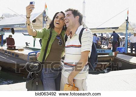 Stock Image - Multi-ethnic couple taking self-portrait at waterfront. Fotosearch