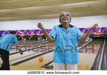 Stock Image - African woman cheering in bowling alley. Fotosearch