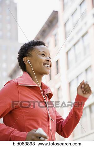 Stock Image - African woman listening to mp3 player while walking outdoors. Fotosearch