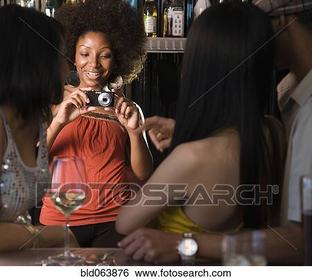 Stock Photograph - African woman photographing friends in nightclub. Fotosearch