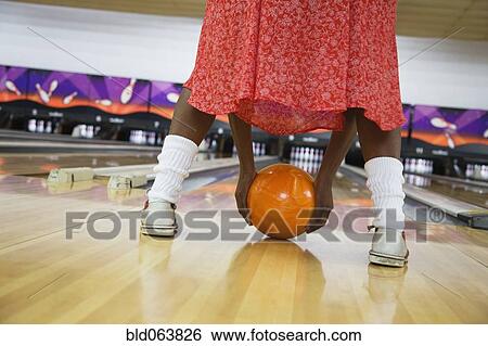 Stock Photograph - African woman playfully rolling bowling ball in bowling alley. Fotosearch