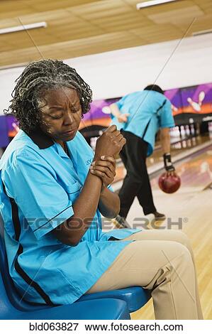 Stock Photo - African woman rubbing aching wrist in bowling alley. Fotosearch