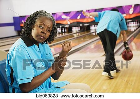 Stock Photo - African woman rubbing aching wrist in bowling alley. Fotosearch
