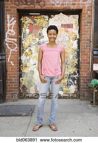 Stock Image - African woman standing near urban doorway. Fotosearch