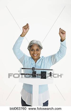 Stock Image - African woman weighing herself on scale. Fotosearch