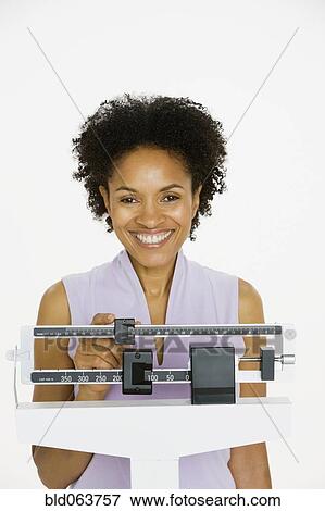 Stock Photo - African woman weighing herself on scale. Fotosearch