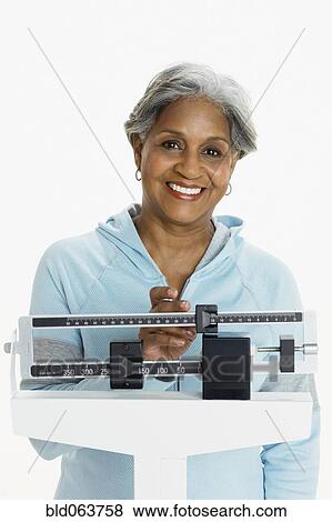 Stock Photo - African woman weighing herself on scale. Fotosearch