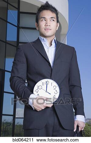 Asian businessman holding clock outdoors View Large Photo Image Stock Image - Asian businessman holding clock outdoors. Fotosearch