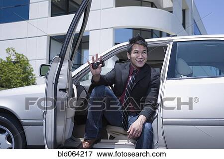 Stock Photo - Asian businessman sitting in car holding cell phone. Fotosearch