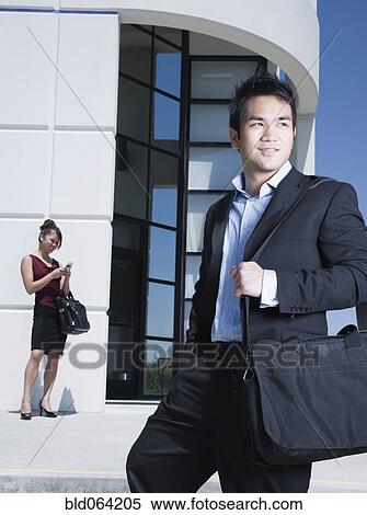 Stock Photography - Asian businessman standing outdoors with briefcase. Fotosearch