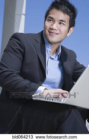 Stock Image - Asian businessman working on laptop outdoors. Fotosearch