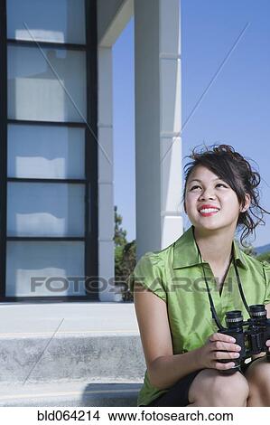 Picture - Asian businesswoman sitting outdoors with binoculars. Fotosearch