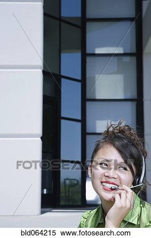 Asian businesswoman sitting outdoors talking on headset View Large Photo Image Stock Photography - Asian businesswoman sitting outdoors talking on headset. Fotosearch