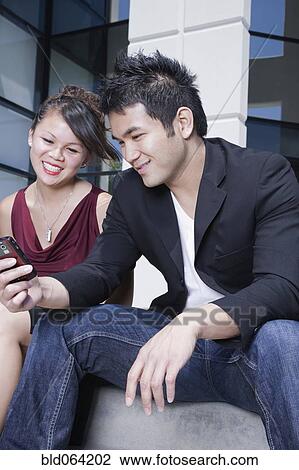 Stock Image - Asian man showing cell phone to girlfriend. Fotosearch