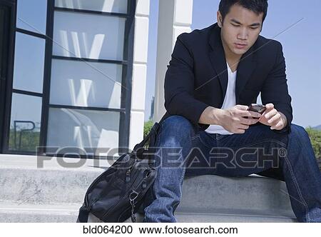 Stock Image - Asian man text messaging with cell phone. Fotosearch