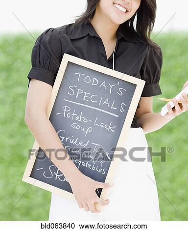 Stock Image - Asian waitress holding chalkboard with day’s specials. Fotosearch