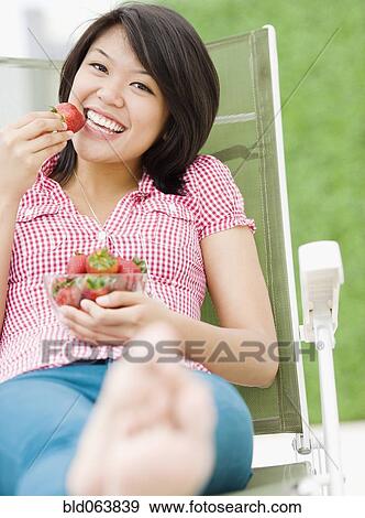 Stock Photo - Asian woman eating strawberries. Fotosearch