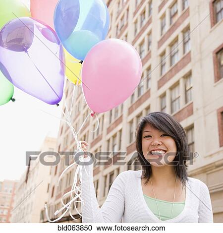 Stock Image - Asian woman holding bunch of balloons. Fotosearch