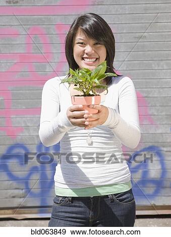 Stock Photo - Asian woman holding potted plant. Fotosearch