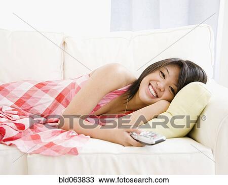 Stock Image - Asian woman laying on sofa watching television. Fotosearch