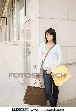 Stock Image - Asian woman outdoors holding shopping bags. Fotosearch