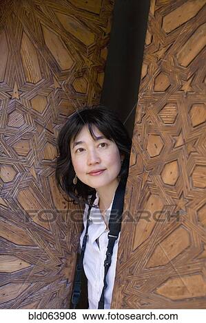 Stock Photo - Asian woman peering out of ornate wooden door. Fotosearch