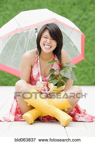 Stock Photo - Asian woman sitting underneath umbrella in rain. Fotosearch