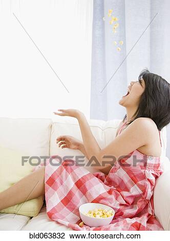 Stock Image - Asian woman tossing popcorn into her mouth. Fotosearch