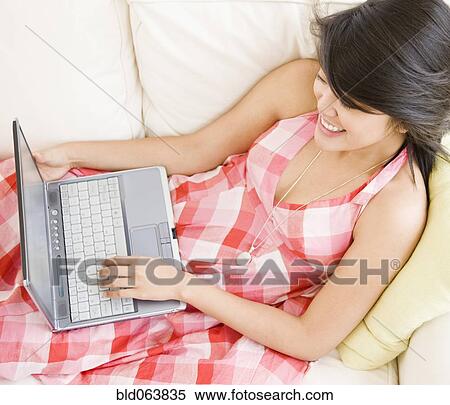 Stock Photography - Asian woman using laptop on sofa. Fotosearch