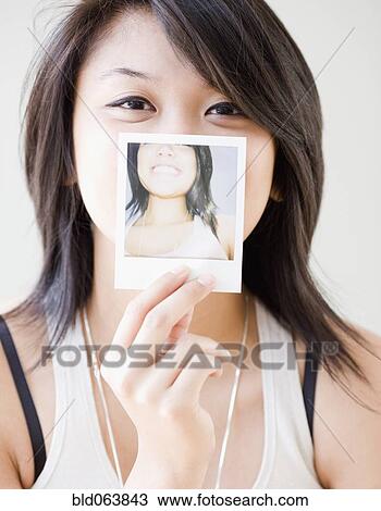 Stock Image - Asian woman with instant photograph of herself. Fotosearch
