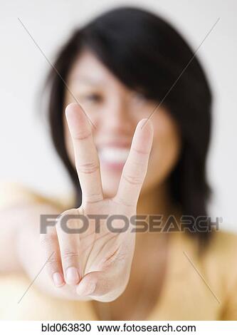 Stock Image - Close up of Asian woman making peace sign. Fotosearch