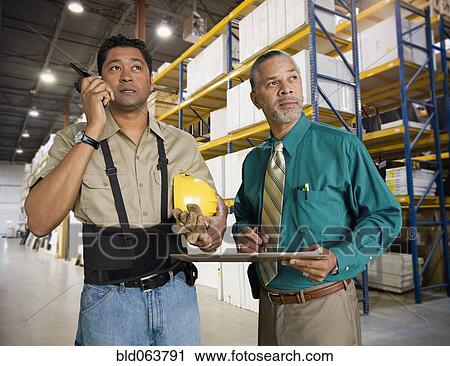 Stock Image - Co-workers standing in warehouse. Fotosearch