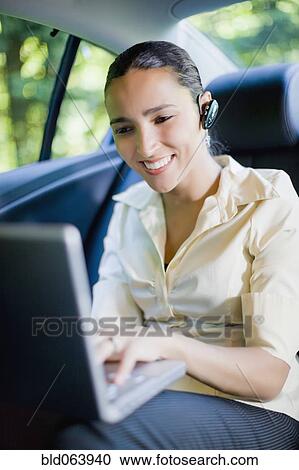 Stock Image - Hispanic businesswoman working in rear seat of car with laptop. Fotosearch
