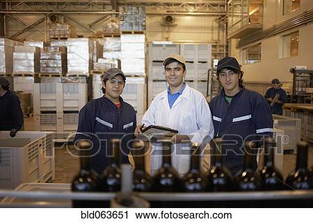 Stock Image - Hispanic men working in bottling factory. Fotosearch