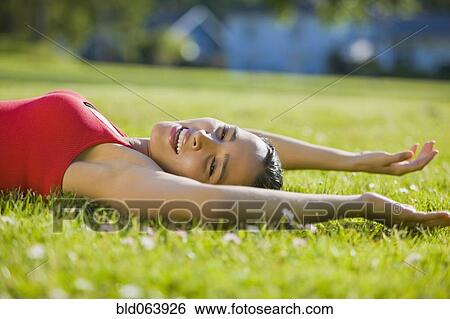 Stock Photograph - Hispanic woman laying in grass stretching. Fotosearch