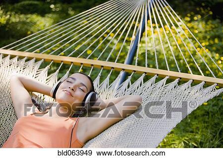 Stock Photo - Hispanic woman laying in hammock listening to headphones. Fotosearch