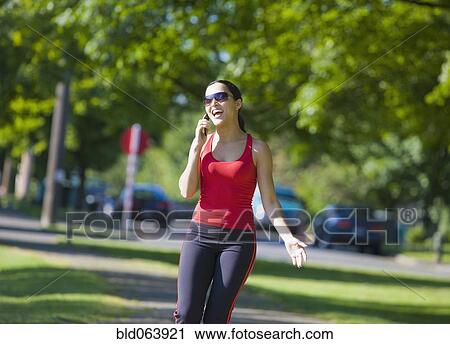 Stock Image - Hispanic woman talking on cell phone in park. Fotosearch