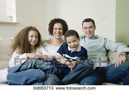 Stock Image - Mixed race family sitting on sofa and smiling. Fotosearch