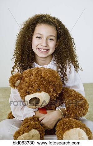 Stock Image - Mixed race girl in nightgown with teddy bear. Fotosearch