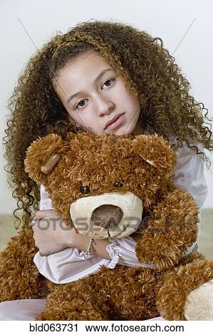 Stock Image - Mixed race girl in nightgown with teddy bear. Fotosearch