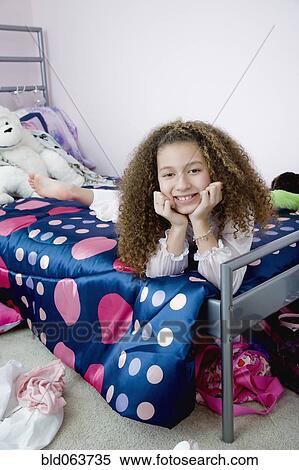 Stock Photography - Mixed race girl laying on bed in bedroom. Fotosearch