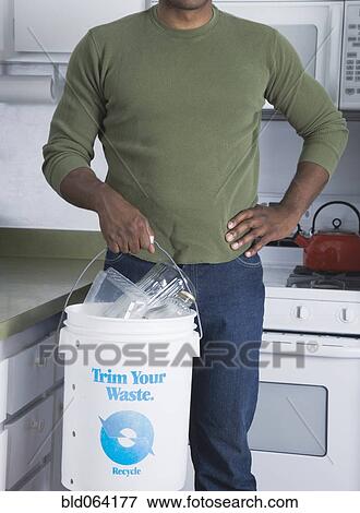 Mixed race man holding recycling bucket in kitchen View Large Photo Image Stock Photo - Mixed race man holding recycling bucket in kitchen. Fotosearch