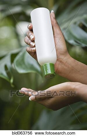 Stock Photograph - Mixed race woman pouring lotion into hand. Fotosearch