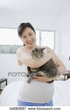 Stock Photo - Pregnant Asian woman holding cat. Fotosearch
